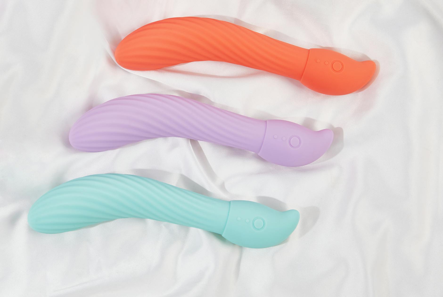 Three colorful clitoral vibrators arranged on white fabric, showcasing smooth texture and design variation