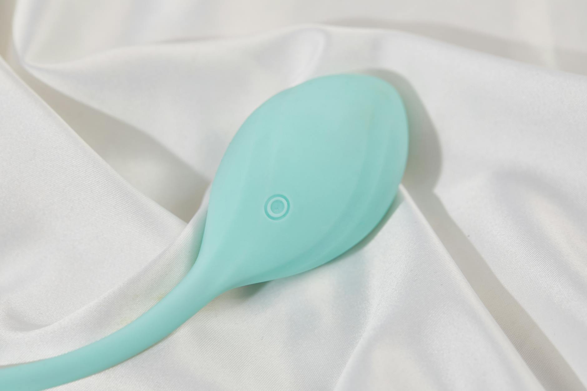 A stylish teal lemon clitoral vibrator on smooth white silk fabric