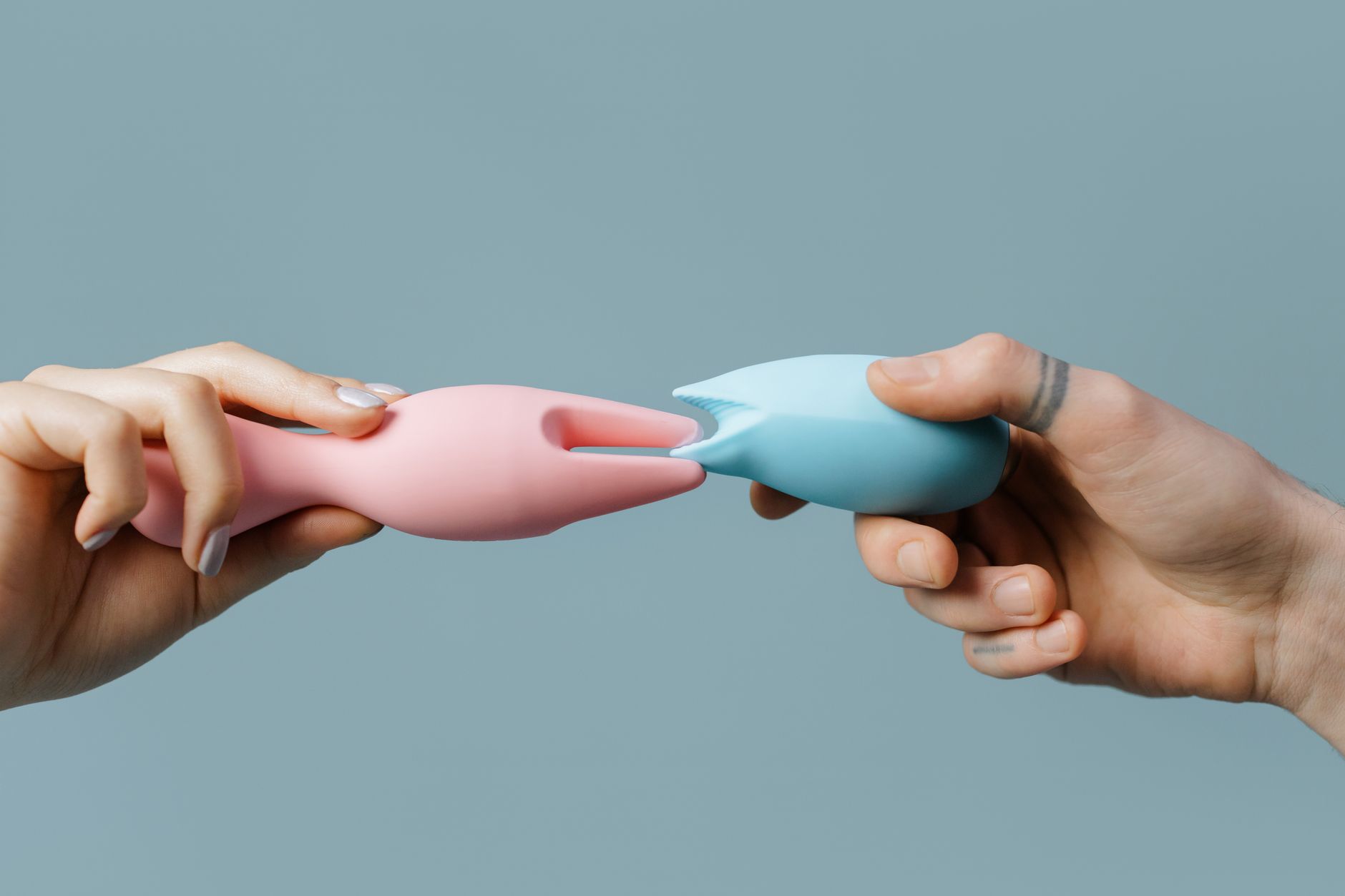 Hands holding pastel silicone adult toys on a soft background