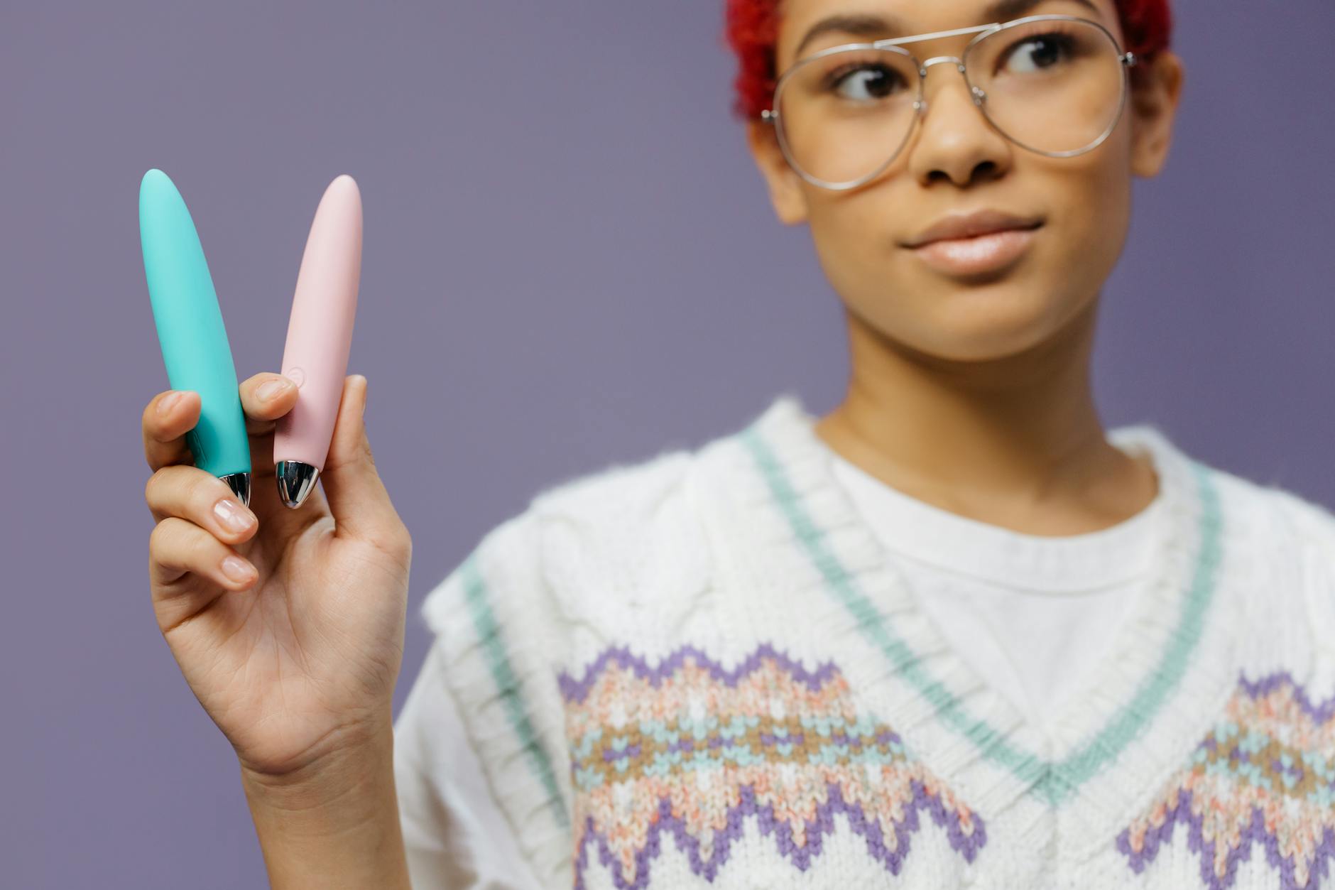 Two colorful adult toys held against a purple background showcasing modern pleasure options