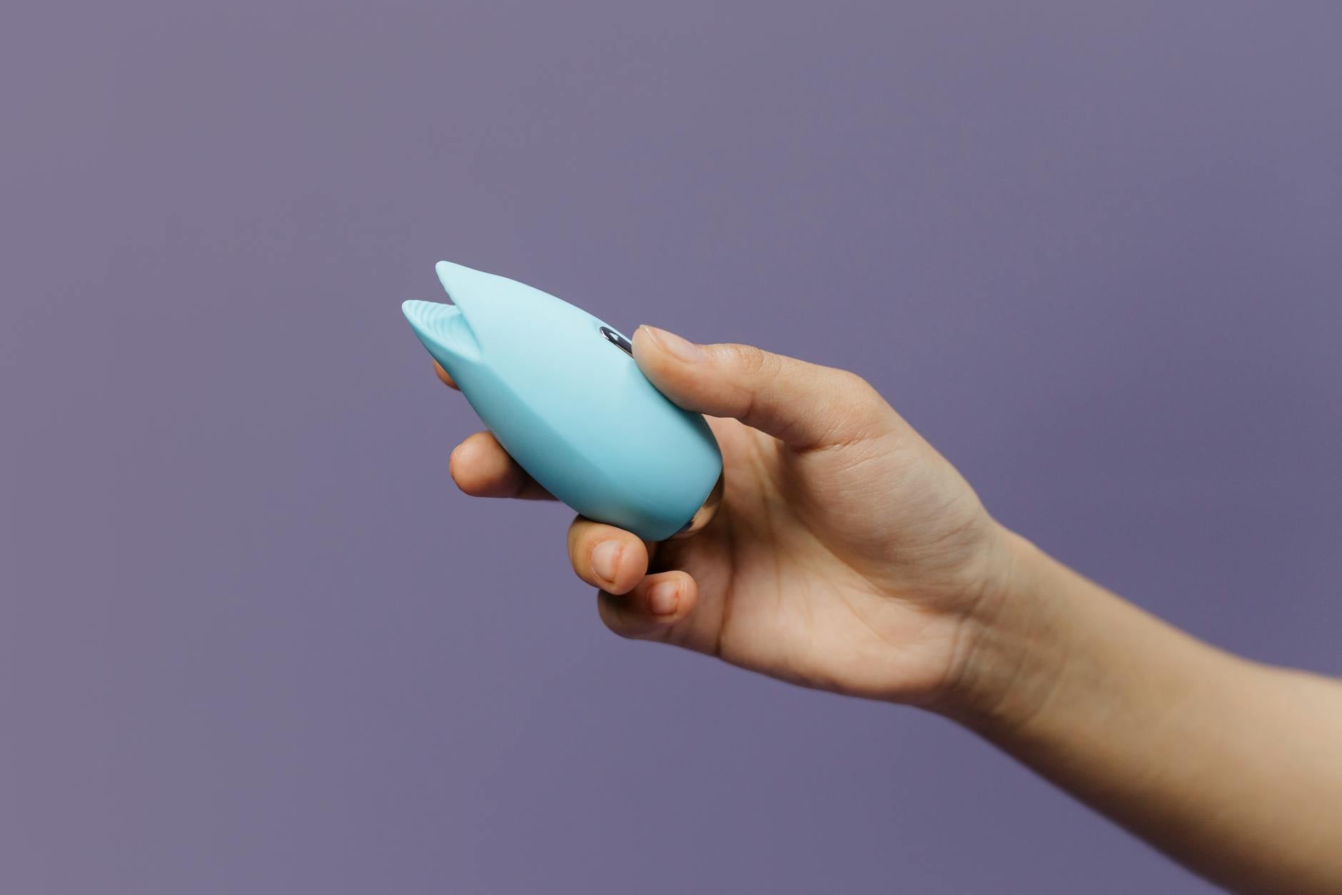 A teal silicone vibrator on smooth white silk fabric, representing gentle postpartum intimacy
